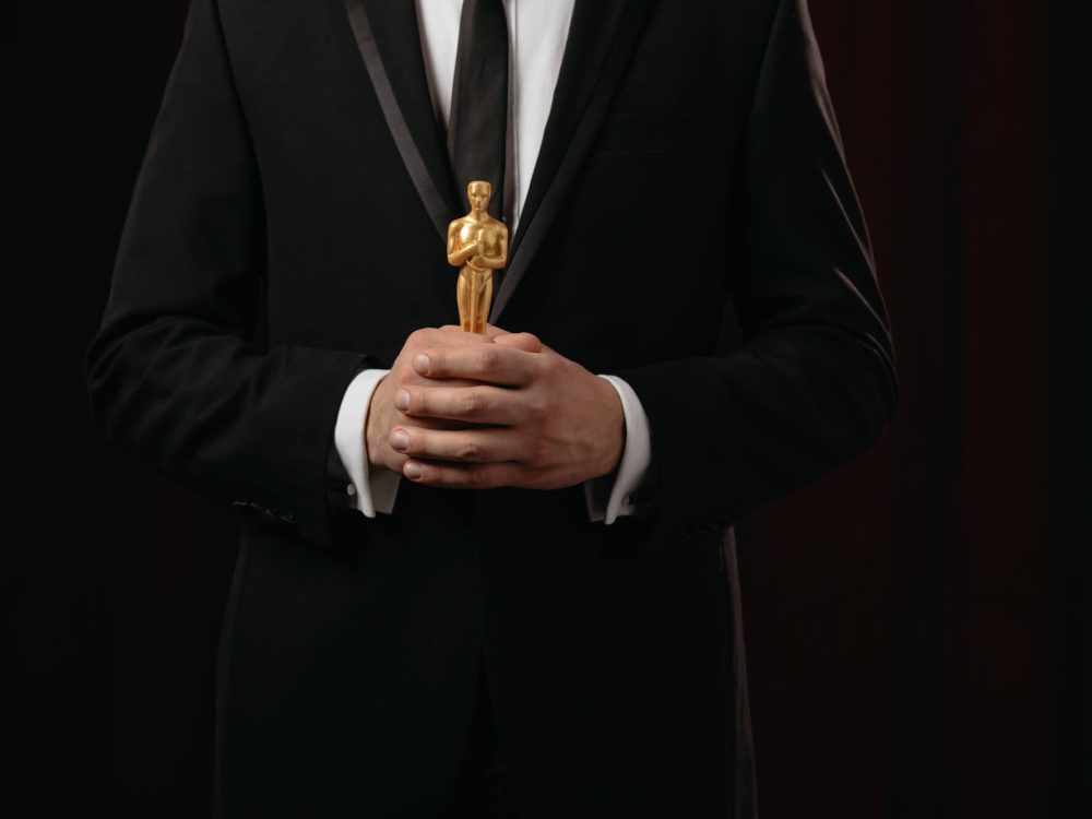 cropped-view-of-man-in-suit-holding-oscar-award-on-dark-background-1.jpg